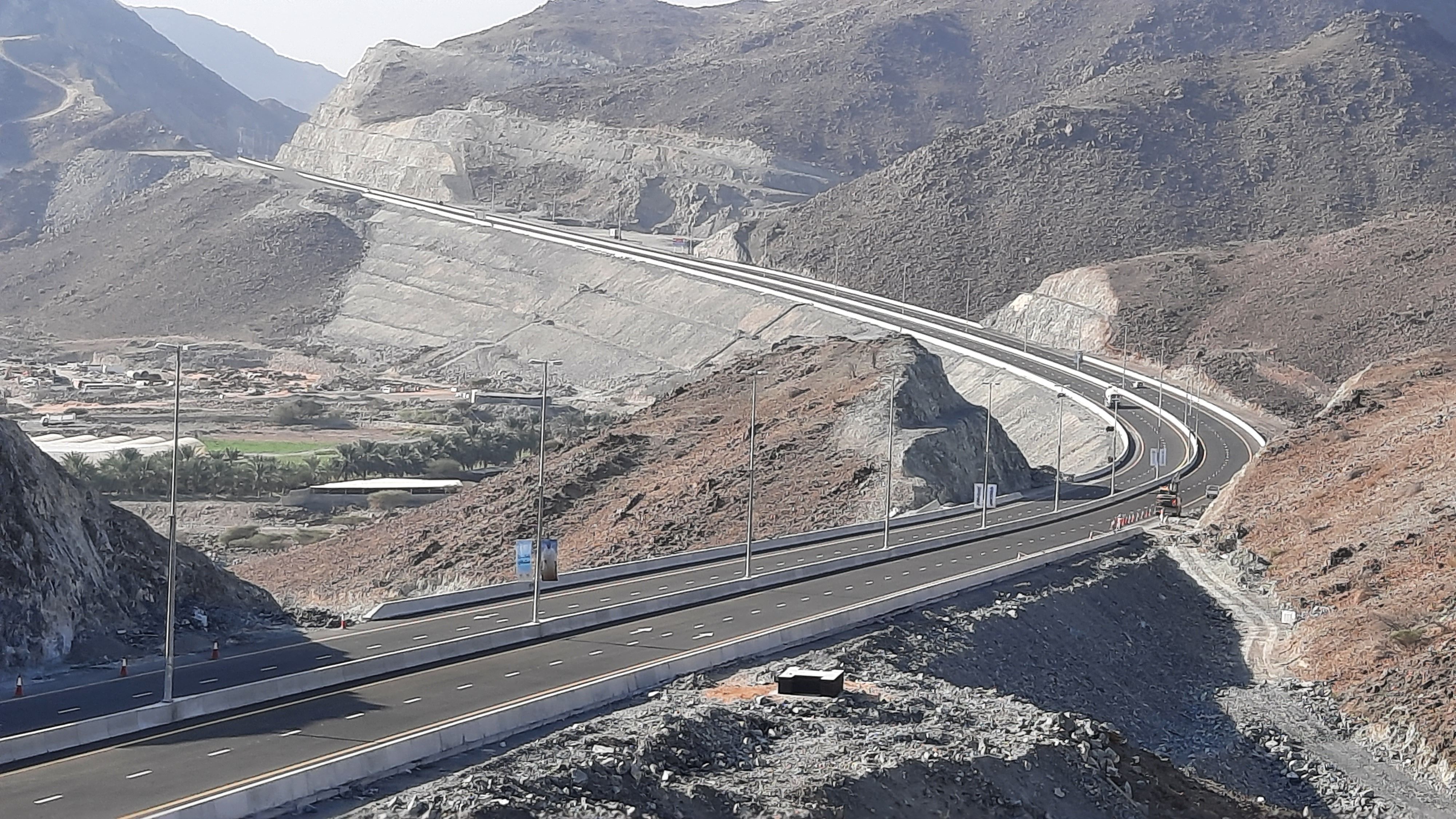 Completed dual carriageway curving through a benched rock cutting in mountainous terrain