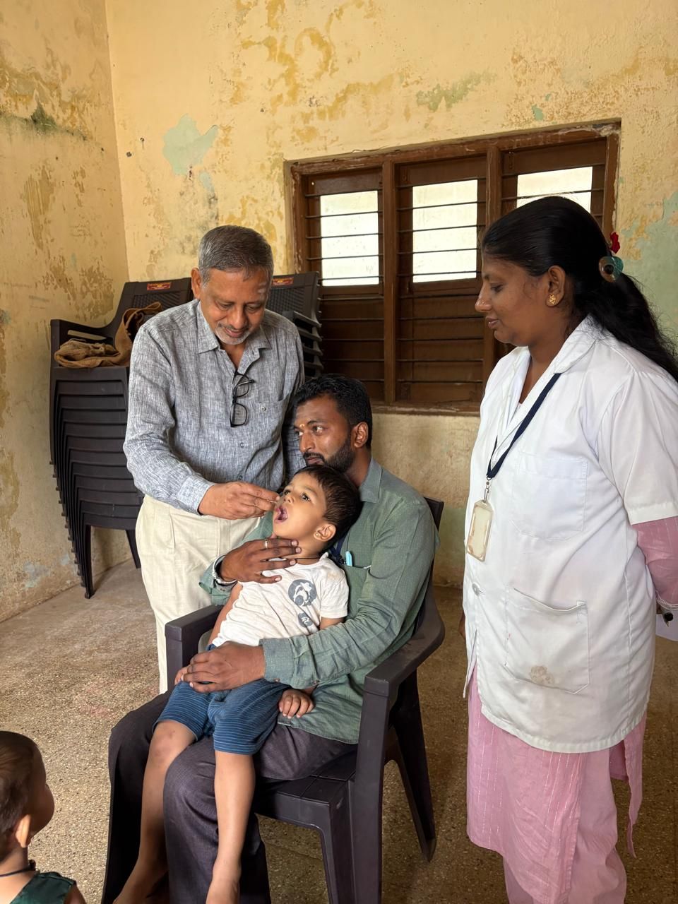 Basavaraj Hiremath administering oral polio vaccine drops to a child at a rural immunisation post, a health worker alongside